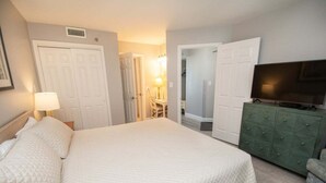 A hotel room with a large bed, a television, a dresser, and a desk with a chair. - Ocean Forest 1006 (Myrtle Beach)