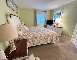 A bedroom with a bed, bedside table, lamp, dresser, mirror, and window with curtains. - Ocean Forest 2011 (Myrtle Beach)