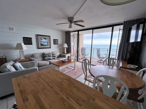 A modern living room with a wooden dining table, grey sofas, and a balcony with a view of the ocean. - Ocean Forest 2011 (Myrtle Beach)