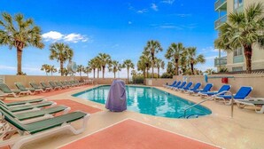 A pool area with sun loungers and palm trees, surrounded by a building with balconies. - Ocean Forest 309 (Myrtle Beach)
