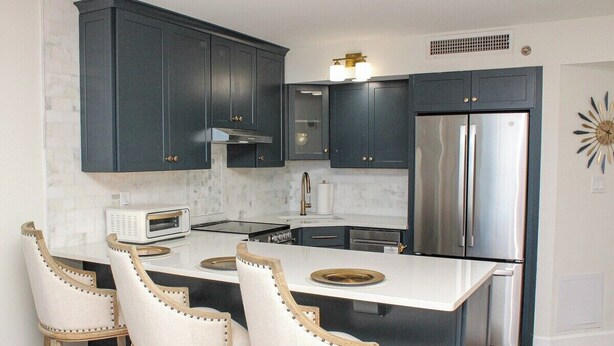 A kitchen with dark cabinets, a stainless steel refrigerator, a microwave, and a central island with bar stools. - Ocean Forest 309 (Myrtle Beach)