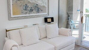 A white sofa with a framed artwork above it, a small table with a remote control, and a glass door leading to an outdoor area. - Ocean Forest 309 (Myrtle Beach)