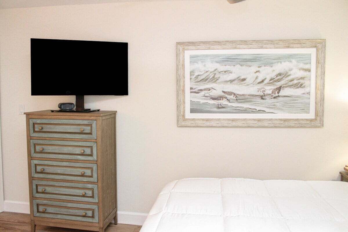 Un dormitorio con una cama, un aparador, un televisor encima del aparador y un cuadro en la pared.