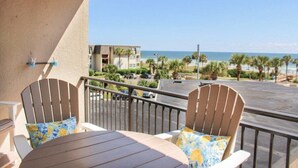 A balcony with two Adirondack chairs and a table, overlooking a beach and a parking area. - Ocean Forest 309 (Myrtle Beach)