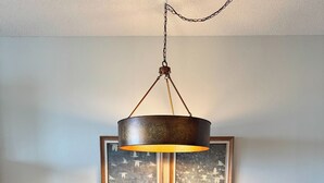 A dining area with a wooden table, black chairs, a hanging light fixture, and a framed artwork on the wall.