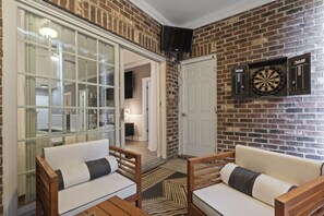 A cozy room with a brick wall, two wooden sofas, a dartboard, and a large window with a view of a hallway. - Oh My Gosh So Posh! Stylish 2BR Condo w/ Glam Decor, Bright Spaces & Relaxed Comfort (Myrtle Beach)