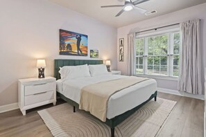 A bedroom with a bed, nightstands, a ceiling fan, a window with curtains, and artwork on the wall. - Oh My Gosh So Posh! Stylish 2BR Condo w/ Glam Decor, Bright Spaces & Relaxed Comfort (Myrtle Beach)