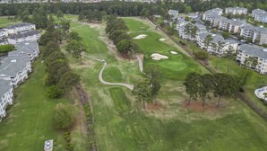 Ett flygbildsbild av ett bostadsområde med en golfbana, flerfamiljshus och en väg.