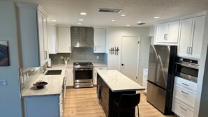 A modern kitchen with white cabinets, stainless steel appliances, a central island, and a wooden floor. - Okeechobee Vacation House (Lake Havasu City)
