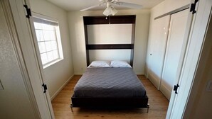 A bedroom with a bed, a ceiling fan, wooden flooring, and a window. - Okeechobee Vacation House (Lake Havasu City)
