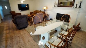 A living room with a glass dining table, wooden chairs, a sofa, a TV, and a fireplace. - Okeechobee Vacation House (Lake Havasu City)