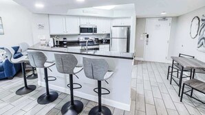 A modern kitchen with white cabinets, a central island with bar stools, a microwave, and a refrigerator. - Oceanview Paradise at the Beach (Myrtle Beach)