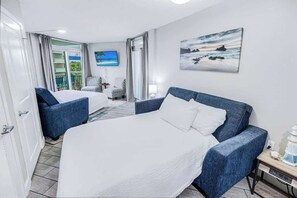 A hotel room with a large bed, two armchairs, a TV, and a painting of a beach scene. - Oceanview Paradise at the Beach (Myrtle Beach)