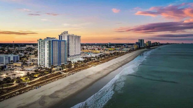 A coastal cityscape with a beachfront hotel, a wide sandy beach, and a clear sky. - Oceanview Paradise at the Beach (Myrtle Beach)