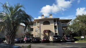 A multi-story hotel with a central entrance, parking lot, and surrounding palm trees. - Cypress Bay Getaway (Little River)