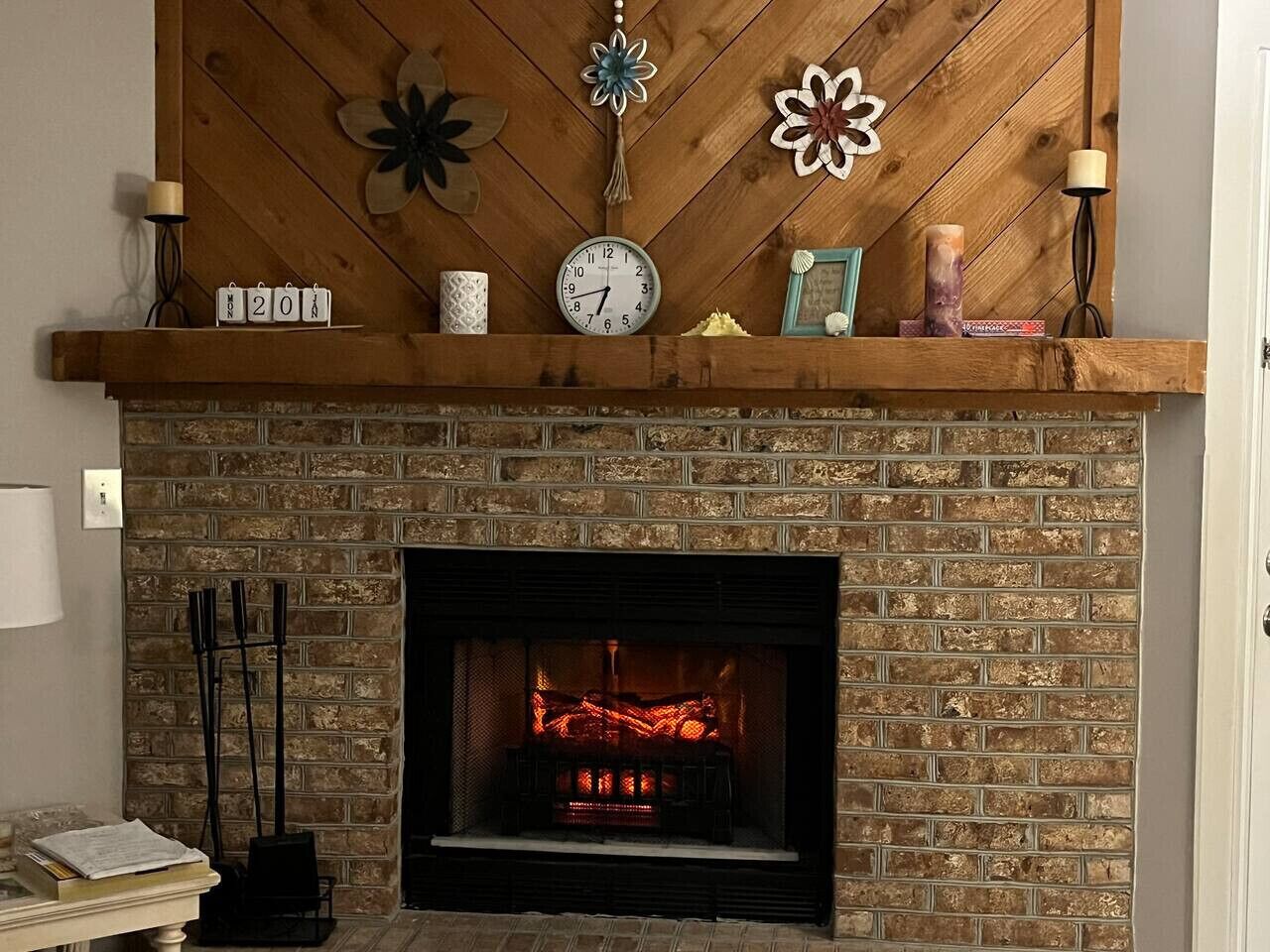 A fireplace with a brick wall, a mantel with decorative items, and a clock.