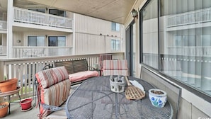 A balcony with a round table, two cushioned chairs, a small statue, and potted plants. - Cypress Bay Getaway (Little River)