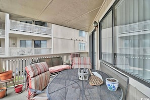 A balcony with a round table, two cushioned chairs, a small statue, and potted plants. - Cypress Bay Getaway (Little River)