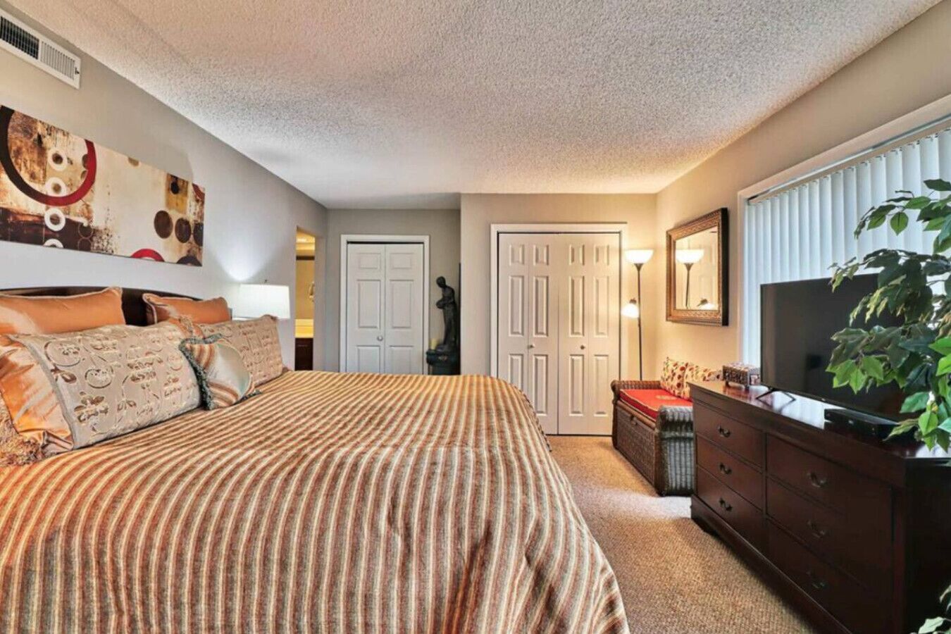 A bedroom with a large bed, a dresser, a television, and a plant.