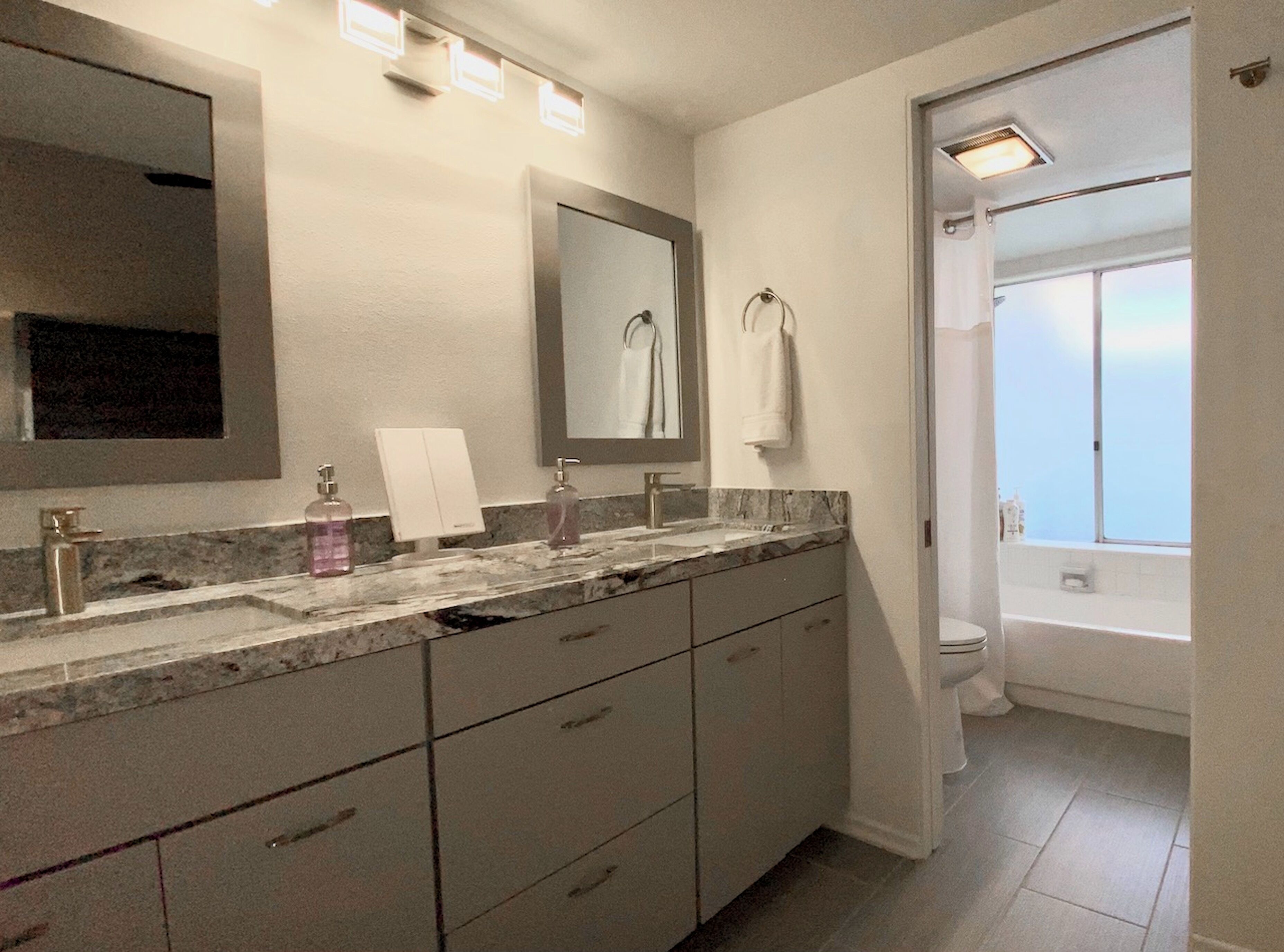 A bathroom with a marble vanity, a large mirror, a toilet, and a window with a view.
