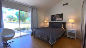 Une chambre à coucher avec un grand lit, deux lampes de chevet, un fauteuil et une fenêtre donnant sur l’extérieur.