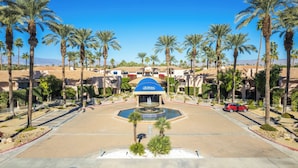 A hotel entrance with a central fountain, palm trees, and a clear blue sky. - Deauville 613 (Palm Springs)