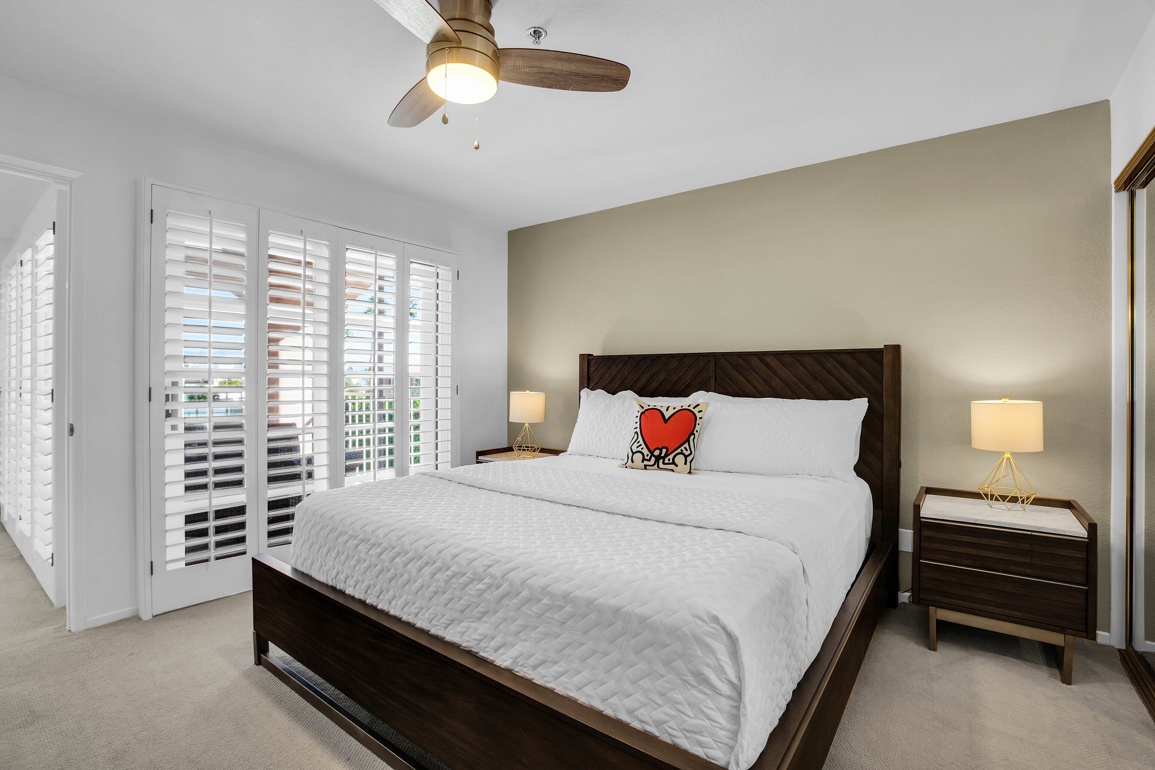 A bedroom with a large bed, a wooden headboard, two bedside tables with lamps, and a ceiling fan.