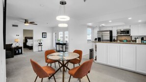 A modern kitchen with white cabinets, stainless steel appliances, and a dining area with orange chairs and a glass table. - Deauville 613 (Palm Springs)