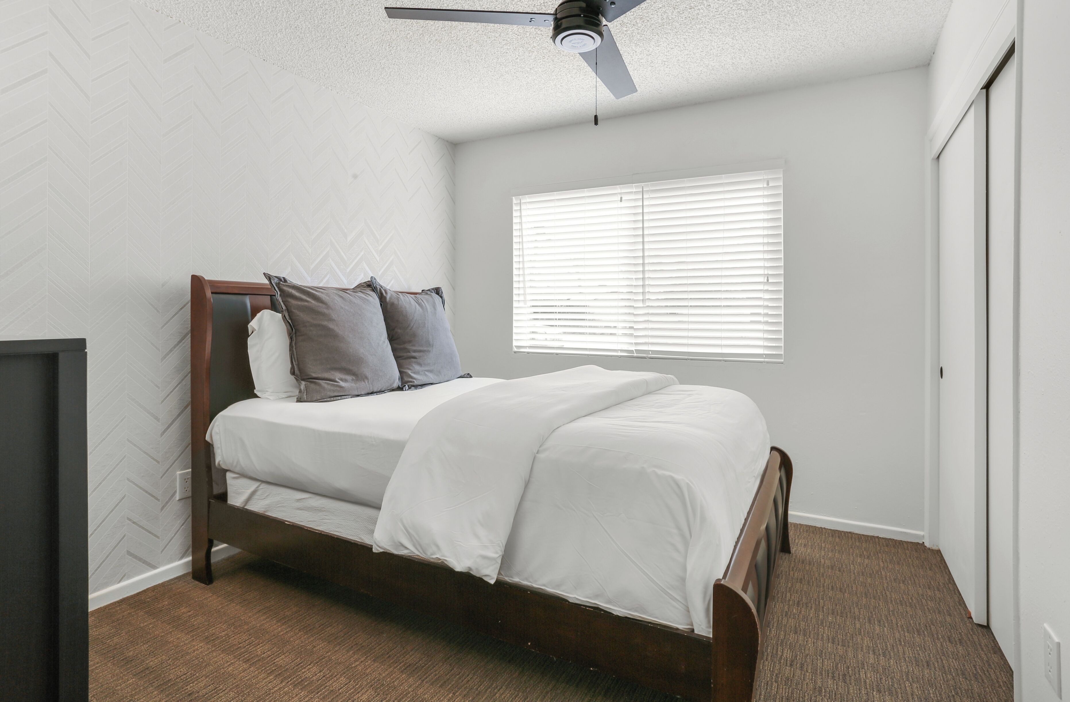 A bedroom with a bed, a ceiling fan, a window with blinds, and a door.