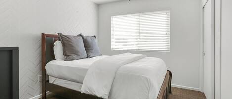 A bedroom with a bed, a ceiling fan, a window with blinds, and a door.