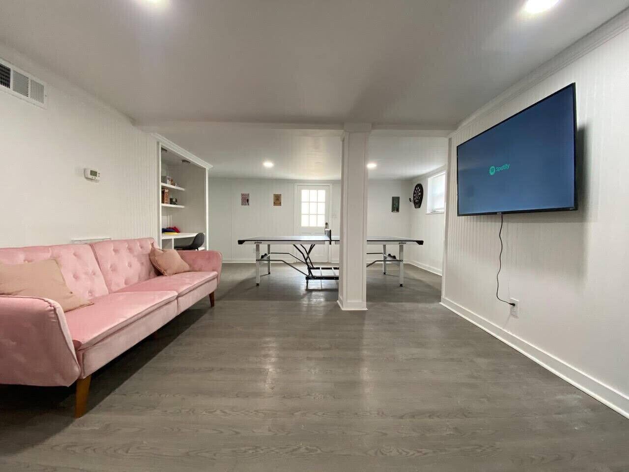A spacious living area with a pink sofa, a dining table, and a flat-screen TV mounted on the wall.