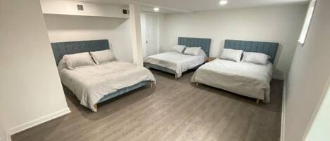 Un dormitorio con tres camas, suelo de madera y paredes blancas.