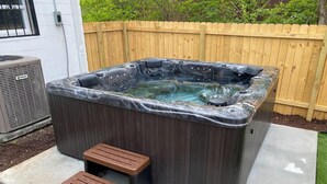 A hot tub with two wooden steps leading up to it, surrounded by a wooden fence and a concrete patio. - New Listing! The Playhouse With Spa Games & More (Nashville)
