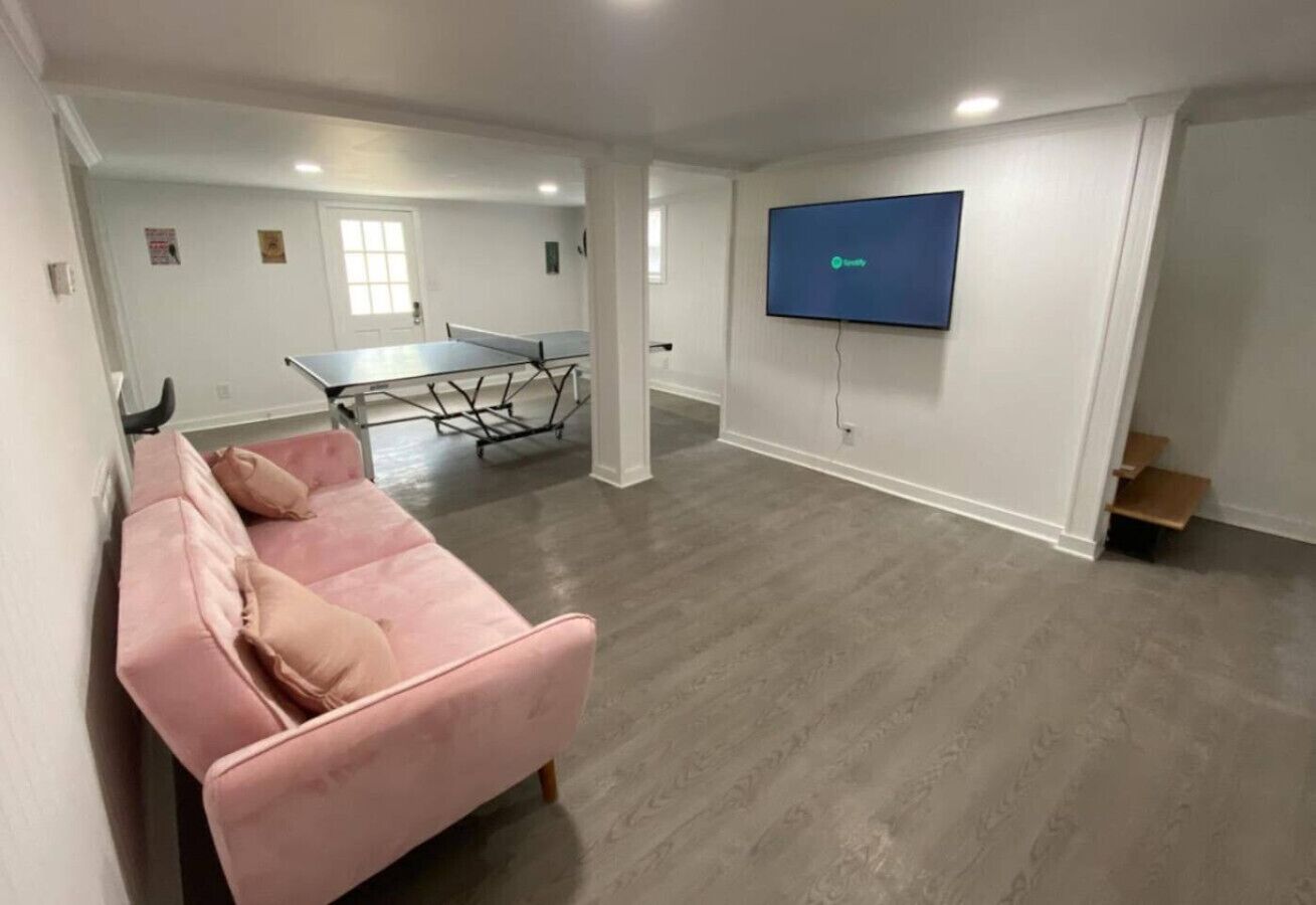 A spacious room with a pink sofa, a ping pong table, and a flat-screen TV mounted on the wall.