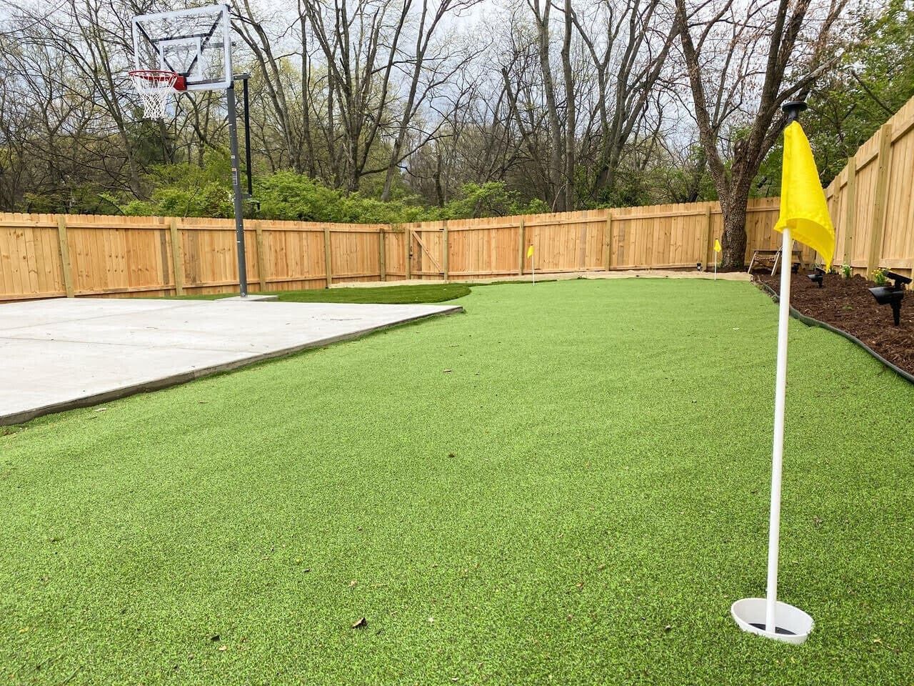Un jardin avec une pelouse artificielle, un panier de basket et un drapeau jaune.