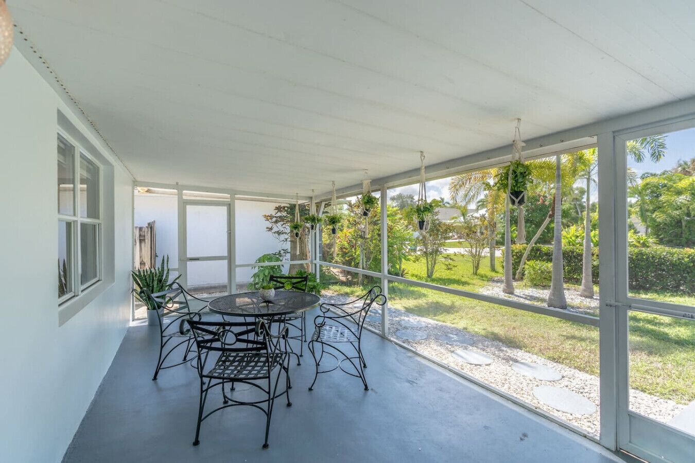 Une terrasse couverte avec une table ronde et des chaises, entourée de grandes fenêtres donnant sur un jardin aménagé.