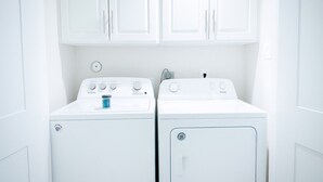 A laundry room with two white front-loading washers and dryers, white cabinets above, and a visible power outlet on the wall. - Beautiful, Pool, Gym, Near Theheights, BBQ (Houston)