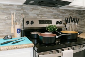 A kitchen with a stove, pots, a blue cutting board, and various utensils. - Beautiful, Pool, Gym, Near Theheights, BBQ (Houston)