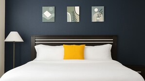 A neatly made bed with white and yellow pillows, a dark headboard, and three framed artworks on the wall. - Beautiful, Pool, Gym, Near Theheights, BBQ (Houston)