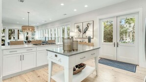 A modern kitchen with white cabinetry, a central island, and a large window. - Coastal Corner Cottage (Santa Rosa Beach)