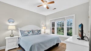 Ein Schlafzimmer mit Bett, Nachttischen, Deckenventilator, Fenster und Fernseher.