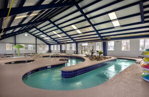 An indoor swimming pool with a blue tiled edge, a roof structure, and a sunlit interior. - Magnolia North 4839-105 (Myrtle Beach)