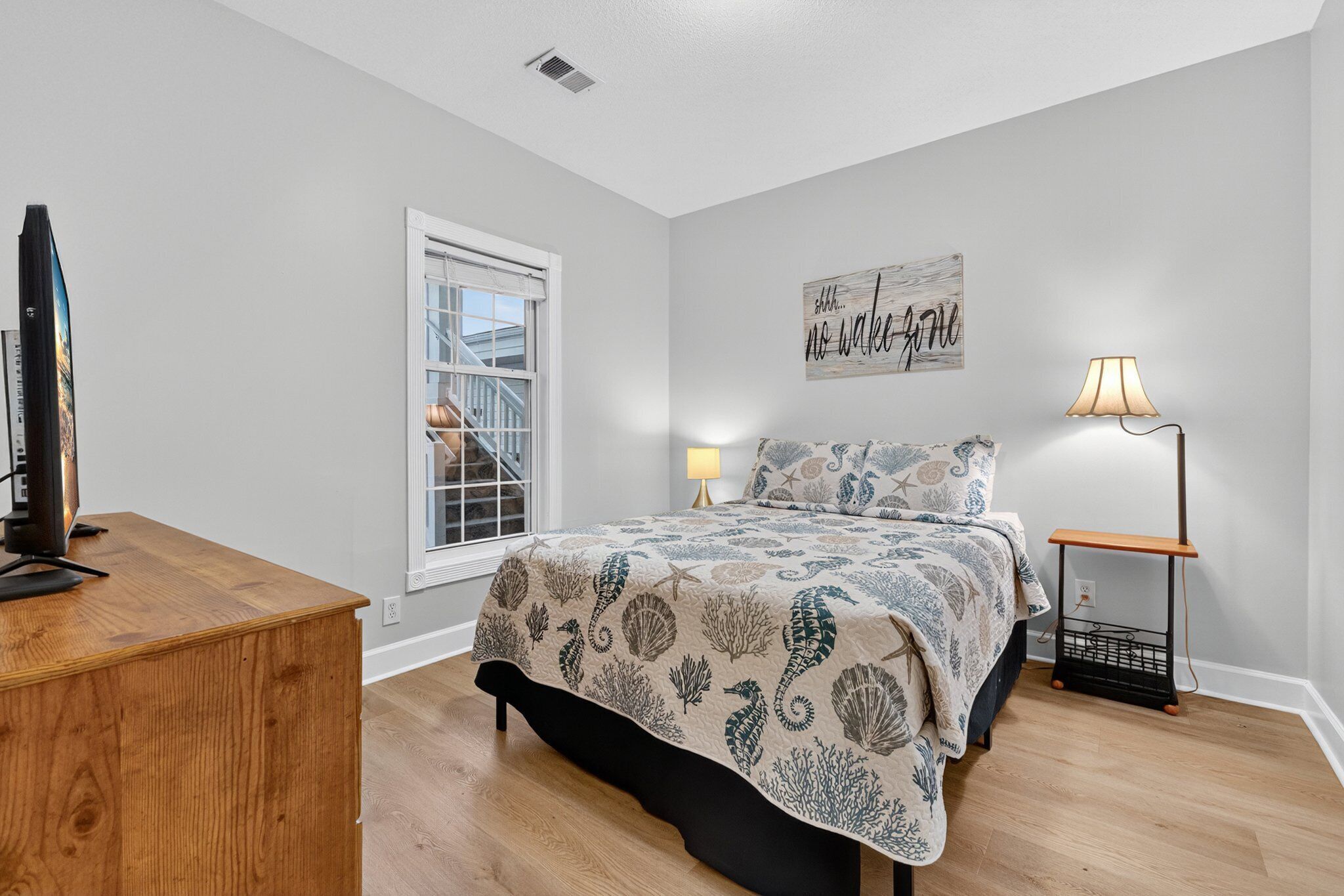A bedroom with a bed, a desk, a lamp, and a window.