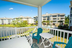 A balcony with a view of a golf course, white outdoor furniture, and a pool. - Magnolia Pointe Luster Leaf 4891-205 (Myrtle Beach)