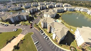 Vue aérienne d’un complexe résidentiel comprenant plusieurs immeubles d’appartements, une route principale et une étendue d’eau.