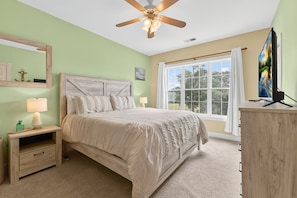 A bedroom with a bed, nightstand, lamp, ceiling fan, window with curtains, and a TV on a stand. - Magnolia Pointe Luster Leaf 4890-303 (Myrtle Beach)