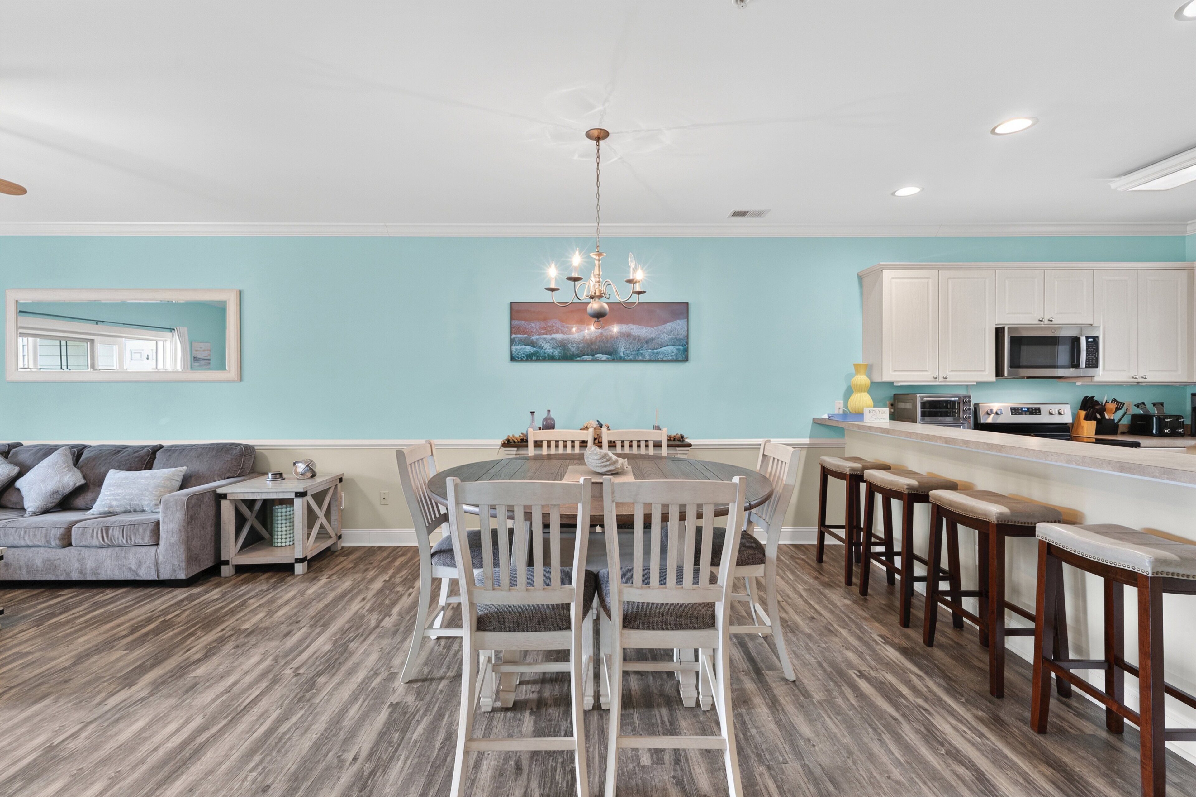 A dining area with a round table and chairs, a kitchen with white cabinets, and a ceiling fan.