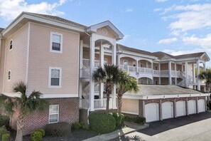 A multi-story building with a brick facade, multiple balconies, and a covered parking area. - Magnolia North 4878-305 (Myrtle Beach)