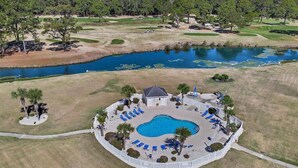 Campo de golf con piscina rodeada de sillas de descanso y palmeras.