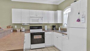 Una cocina con armarios blancos, microondas, estufa, horno, lavavajillas y refrigerador.